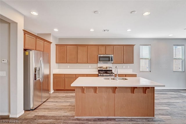 kitchen with sink, a kitchen breakfast bar, an island with sink, stainless steel appliances, and light hardwood / wood-style floors