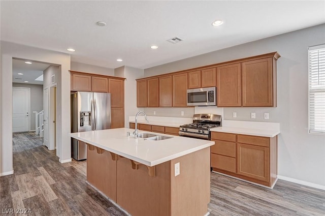 kitchen with sink, hardwood / wood-style flooring, a breakfast bar area, appliances with stainless steel finishes, and an island with sink