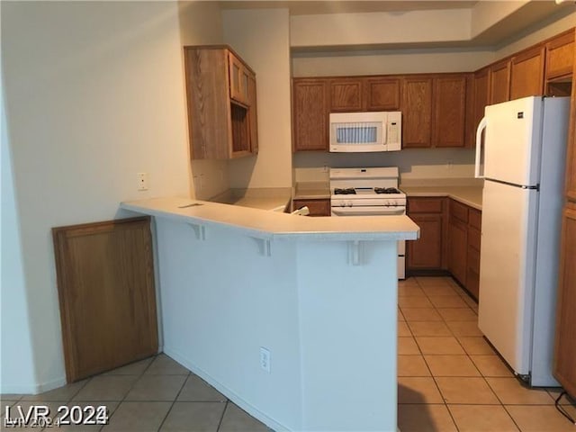 kitchen with a kitchen breakfast bar, white appliances, light tile patterned floors, and kitchen peninsula