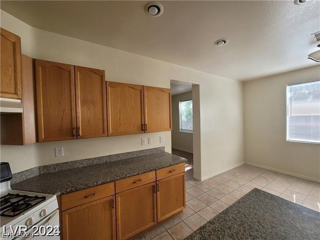 kitchen with dark stone countertops, light tile patterned floors, white range with gas cooktop, and a healthy amount of sunlight