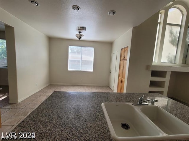 kitchen featuring light tile patterned flooring, dark stone counters, and sink