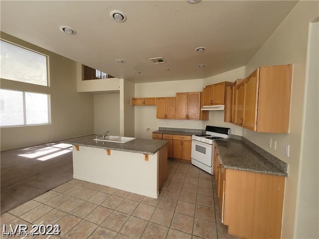 kitchen featuring light tile patterned floors, white gas stove, dark stone countertops, a kitchen island, and sink