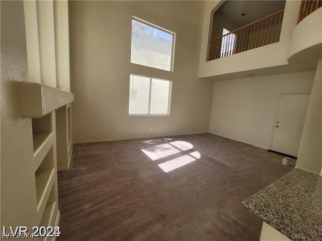 unfurnished living room with a towering ceiling and dark carpet