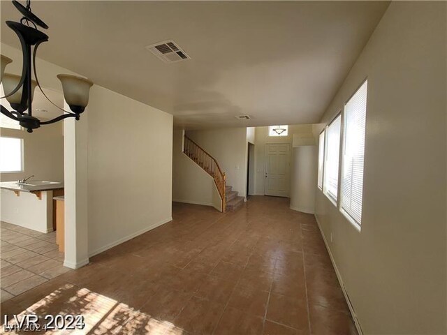 unfurnished living room with tile patterned flooring, sink, and an inviting chandelier