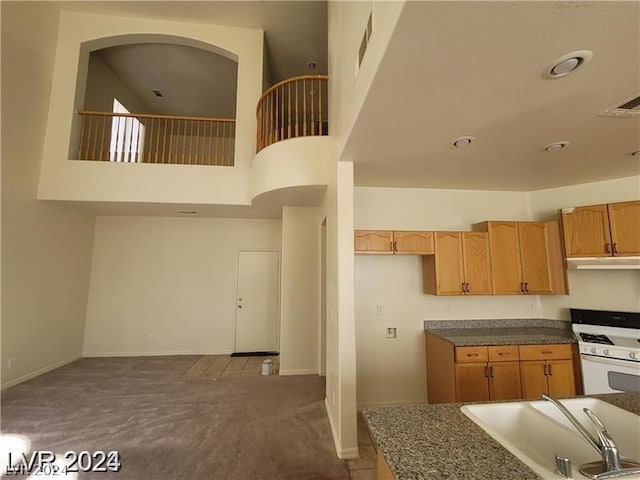 kitchen with light brown cabinets, white range with gas cooktop, a towering ceiling, carpet flooring, and sink