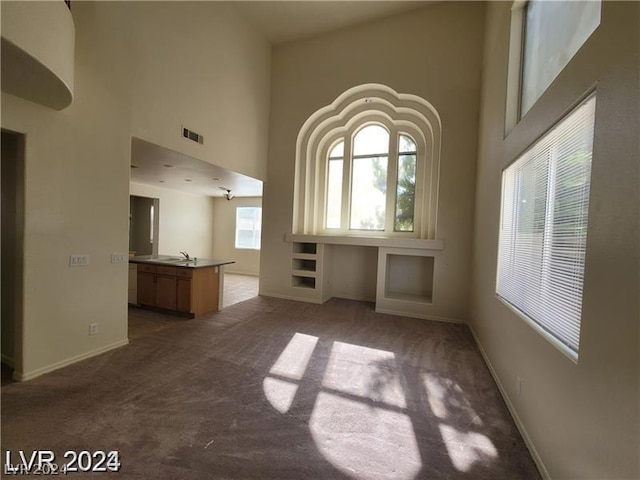 unfurnished living room featuring sink, carpet, built in shelves, and a towering ceiling