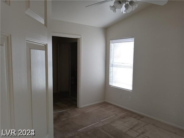 unfurnished room featuring lofted ceiling, dark colored carpet, a healthy amount of sunlight, and ceiling fan