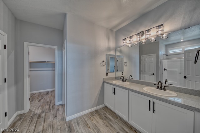 bathroom with a textured ceiling, wood-type flooring, double sink vanity, and an enclosed shower