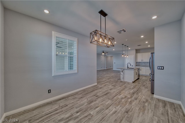 unfurnished dining area with sink, ceiling fan with notable chandelier, and light hardwood / wood-style floors