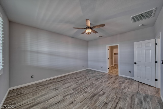 unfurnished bedroom with a closet, a spacious closet, wood-type flooring, and ceiling fan