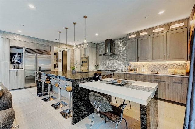 kitchen featuring a spacious island, appliances with stainless steel finishes, wall chimney exhaust hood, light tile patterned floors, and a breakfast bar area