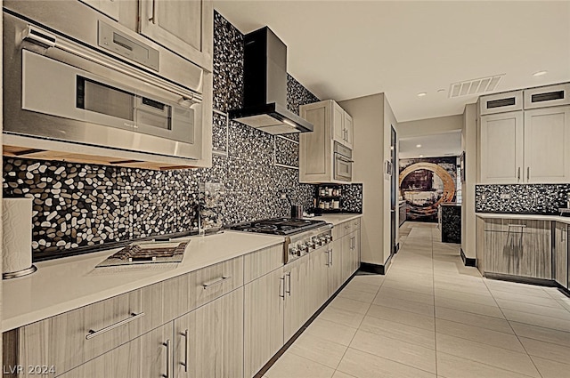 kitchen featuring light brown cabinetry, backsplash, light tile patterned floors, wall chimney exhaust hood, and stainless steel gas cooktop