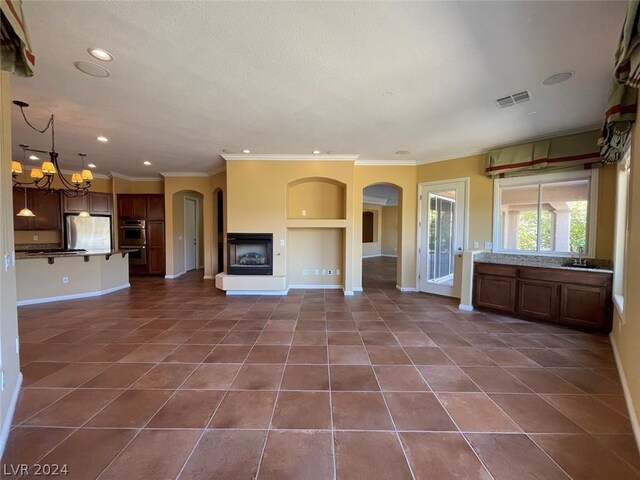 unfurnished living room featuring dark tile patterned floors, crown molding, sink, and a chandelier