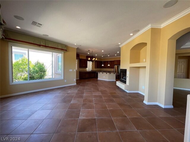 unfurnished living room with crown molding, built in features, dark tile patterned flooring, and an inviting chandelier