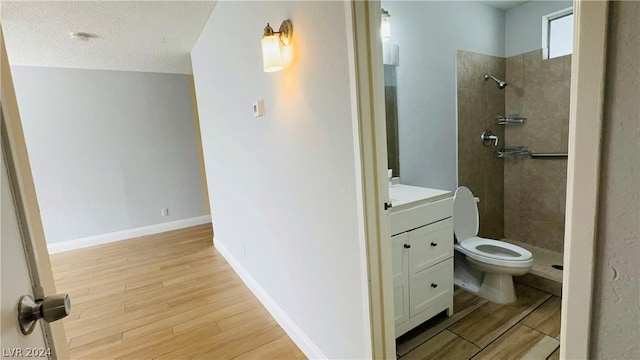 bathroom with tiled shower, wood-type flooring, vanity, and toilet