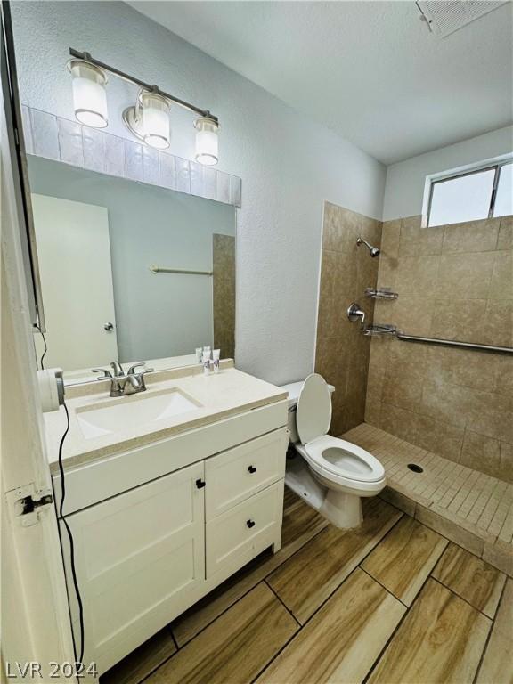 bathroom with hardwood / wood-style floors, vanity, toilet, a textured ceiling, and a tile shower