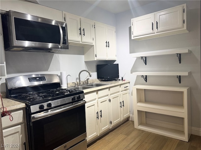 kitchen with appliances with stainless steel finishes, sink, white cabinets, and light wood-type flooring