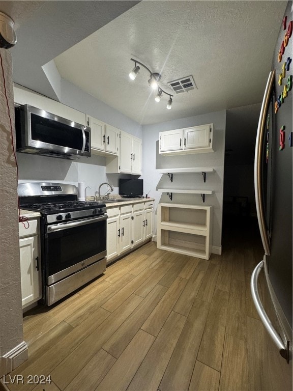 kitchen with white cabinets, light wood-type flooring, stainless steel appliances, and a textured ceiling