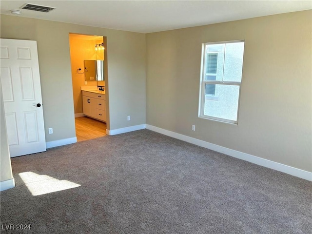 unfurnished bedroom featuring light carpet, ensuite bath, and sink