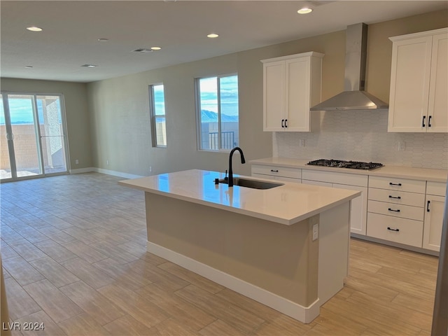 kitchen featuring stainless steel gas stovetop, sink, a kitchen island with sink, and wall chimney range hood