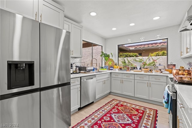 kitchen with stainless steel appliances, light hardwood / wood-style floors, sink, backsplash, and ventilation hood