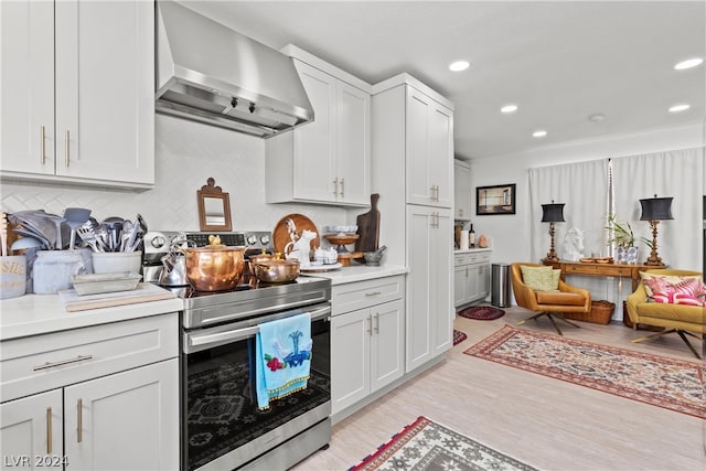 kitchen featuring electric stove, white cabinets, wall chimney exhaust hood, backsplash, and light hardwood / wood-style flooring