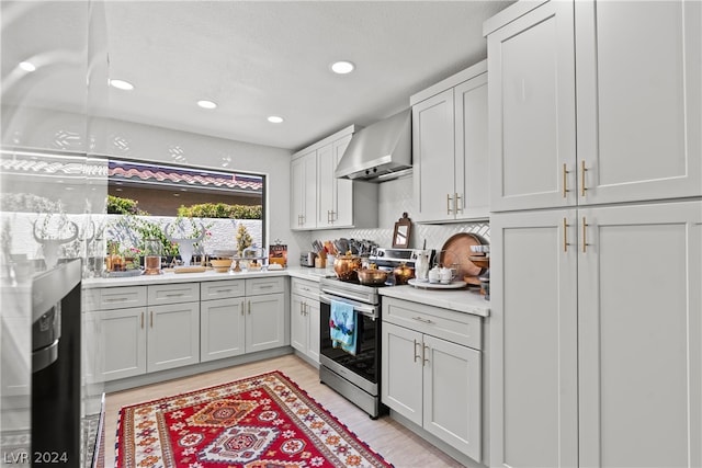 kitchen with light wood-type flooring, stainless steel electric range, decorative backsplash, and wall chimney range hood