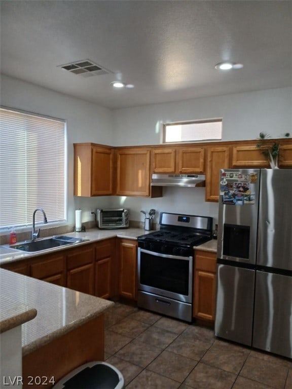 kitchen featuring stainless steel appliances, visible vents, brown cabinetry, a sink, and under cabinet range hood