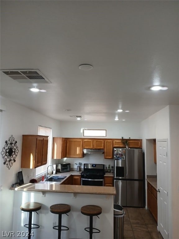 kitchen featuring a peninsula, a sink, visible vents, appliances with stainless steel finishes, and a kitchen bar