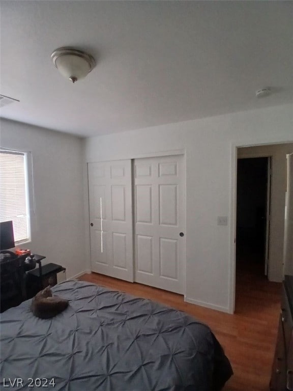 bedroom with a closet, visible vents, baseboards, and wood finished floors