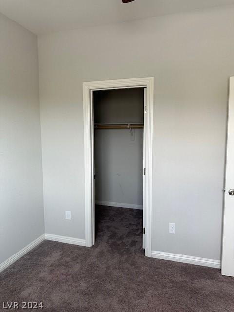 unfurnished bedroom featuring dark colored carpet, a walk in closet, and a closet