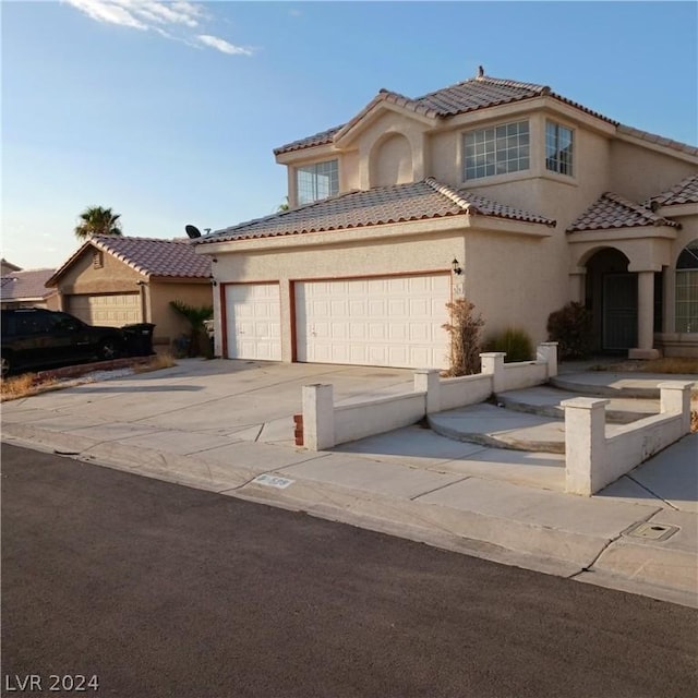 mediterranean / spanish-style home with a garage, driveway, a tiled roof, and stucco siding