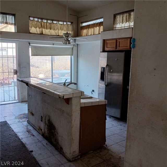 kitchen featuring ceiling fan, stainless steel fridge with ice dispenser, sink, tile counters, and light tile patterned floors