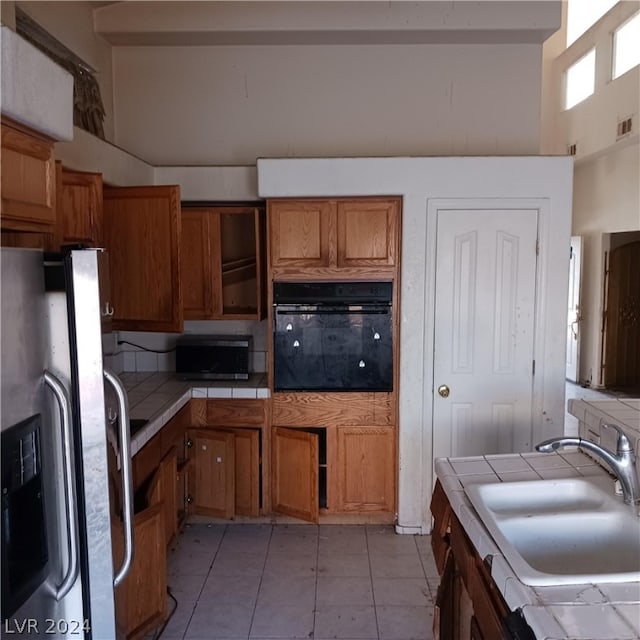 kitchen with light tile patterned flooring, a high ceiling, stainless steel appliances, sink, and tile counters