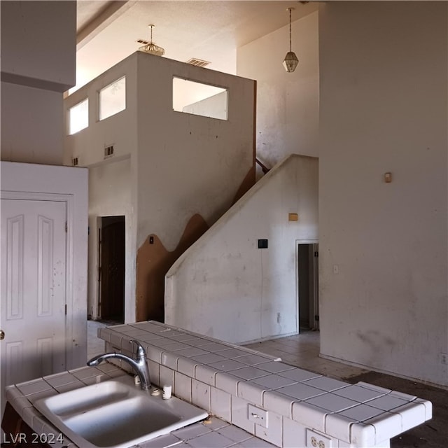 kitchen with high vaulted ceiling, sink, tile countertops, and decorative light fixtures