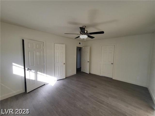 unfurnished bedroom with ceiling fan, dark wood-type flooring, and two closets