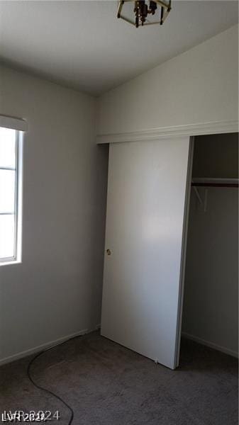 unfurnished bedroom featuring dark carpet, a closet, and a notable chandelier