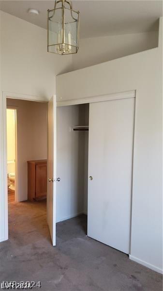 unfurnished bedroom featuring dark carpet, a closet, a notable chandelier, and vaulted ceiling