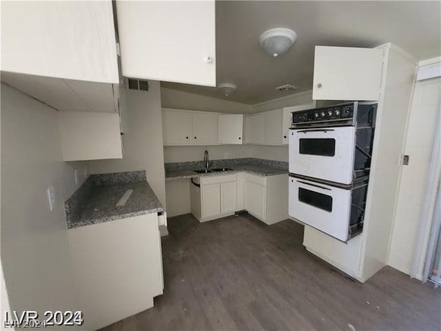 kitchen with white cabinets, dark hardwood / wood-style flooring, double oven, dark stone counters, and sink