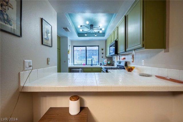 kitchen with visible vents, green cabinetry, appliances with stainless steel finishes, a tray ceiling, and a sink