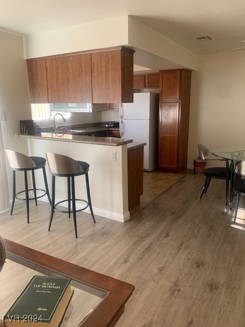 kitchen featuring a breakfast bar area, white refrigerator, sink, kitchen peninsula, and hardwood / wood-style flooring