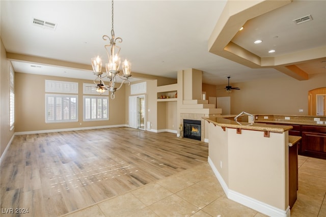 kitchen with decorative light fixtures, ceiling fan with notable chandelier, a kitchen bar, and light wood-type flooring