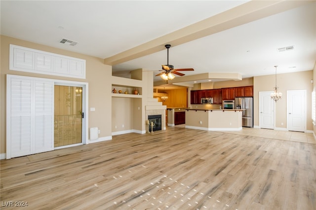 unfurnished living room with built in shelves, ceiling fan with notable chandelier, a fireplace, and light wood-type flooring