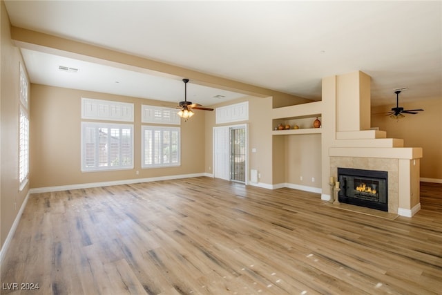 unfurnished living room featuring a tiled fireplace, ceiling fan, light wood-type flooring, and a wealth of natural light