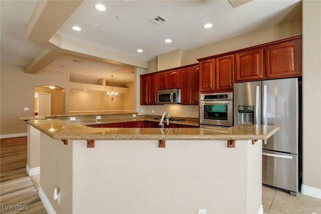 kitchen with a breakfast bar area, light hardwood / wood-style flooring, hanging light fixtures, kitchen peninsula, and stainless steel appliances