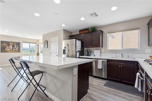 kitchen featuring sink, a center island, light hardwood / wood-style floors, appliances with stainless steel finishes, and a breakfast bar