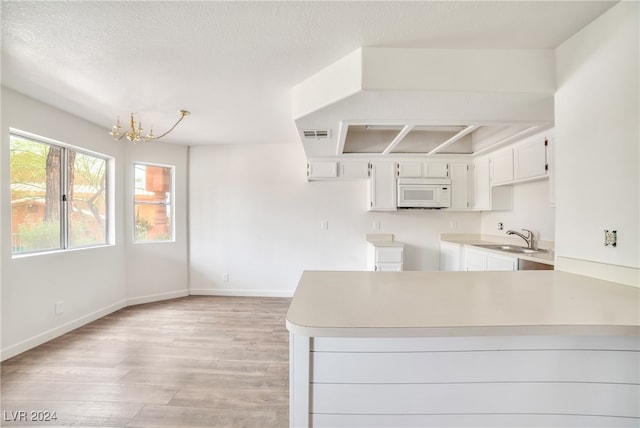 kitchen with light hardwood / wood-style flooring, a chandelier, kitchen peninsula, white cabinets, and sink