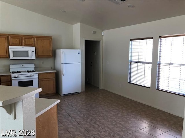 kitchen featuring white appliances, light tile patterned floors, lofted ceiling, and a breakfast bar area