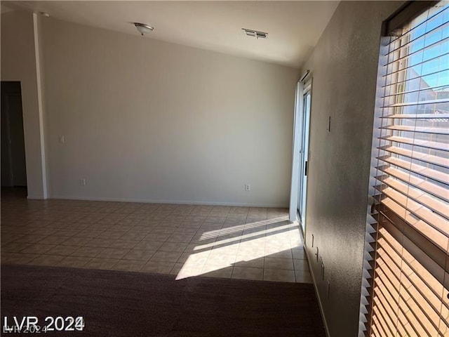 tiled empty room featuring lofted ceiling