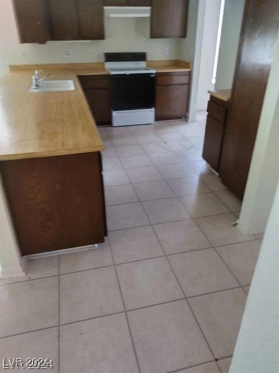 kitchen featuring light tile patterned floors, white stove, dark brown cabinetry, and sink